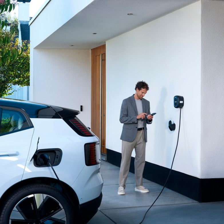 Coche eléctrico blanco conectado a un Wallbox junto a una vivienda.
